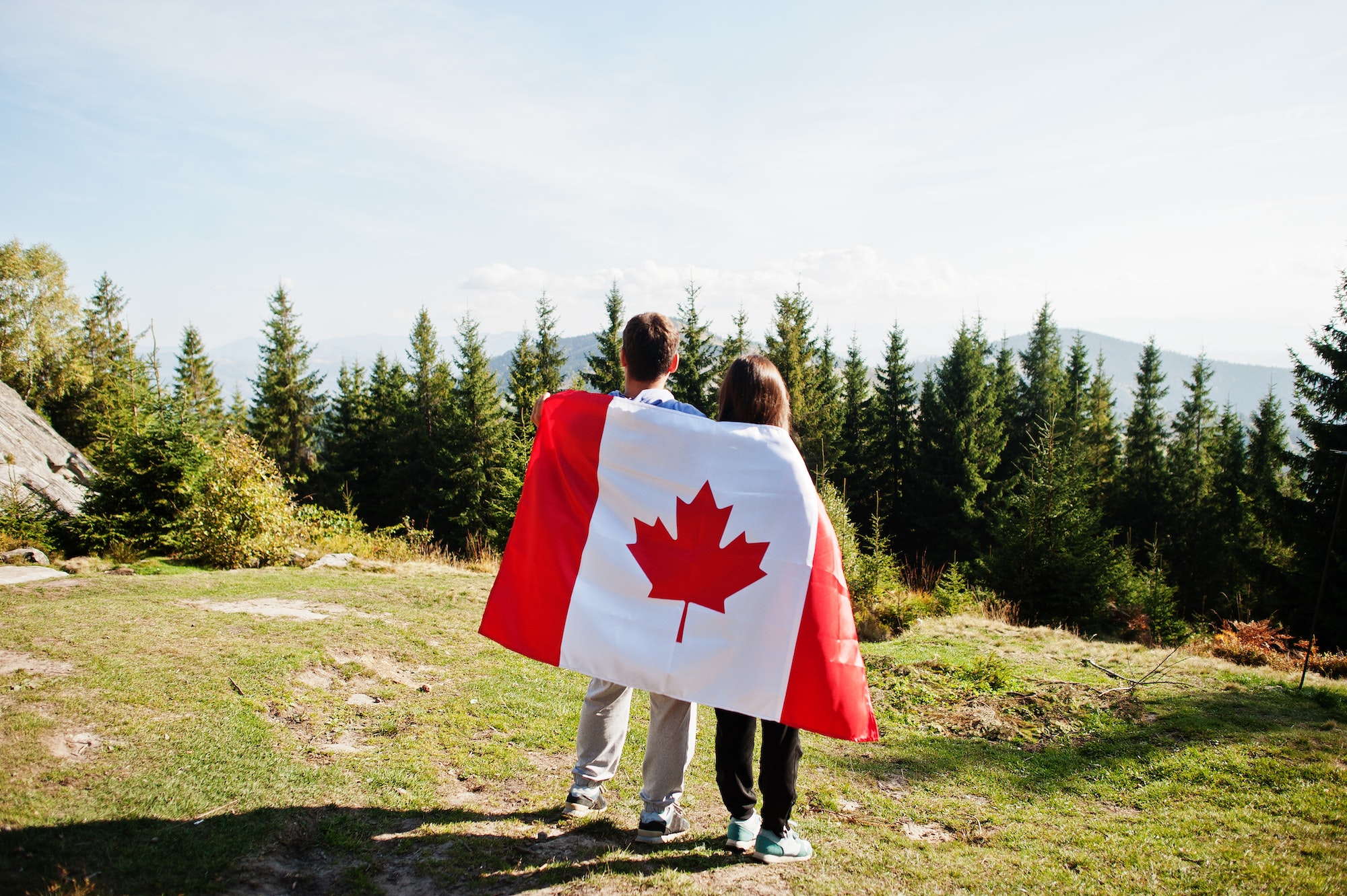 Happy Canada Day. Couple with large Canadian flag celebration in mountains.