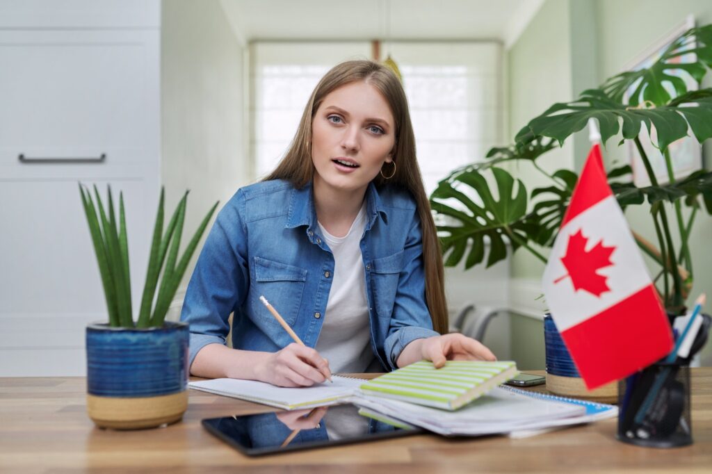 Online training, female teenager sitting at home looking at webcam, Canadian flag on table