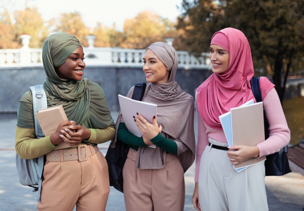 Three Muslim Female Students In Hijab Holding Books Standing Outdoors
